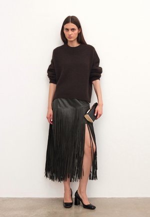 Pull en tricot marron avec des manches retroussées ; jupe en cuir noir avec des détails à franges et une fente sur le côté ; chaussures à talons hauts noires ; petite pochette.
