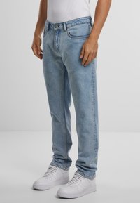 Lyseblå denimjeans med rett passform, fem-lomme-design og metallknapplukking. Utført med hvite joggesko og en tettsittende hvit tanktop.