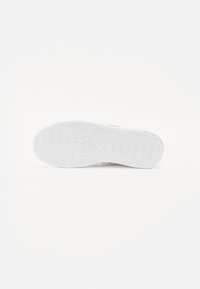 Sola di sneaker bianca con un motivo di presa testurizzato, forma arrotondata e dettaglio di branding discreto vicino al tallone. Materiale in gomma liscia.