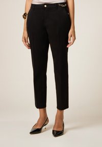 Pantaloni neri su misura con una vestibilità slim, caratterizzati da un dettaglio in catena dorata in vita e un tessuto liscio con un delicato lucido.