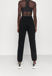 Svart sportbh och matchande joggers, med en figurnära design, elastisk midja och avsmalnande muddar, tillsammans med vita sneakers.