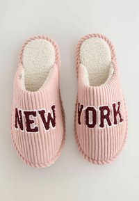 Ein Paar pinke Cord-Stoff Hausschuhe mit weißem Fleece-Futter und "NEW YORK" in dunklem Rot auf der Oberseite, vor einem hellen Hintergrund.