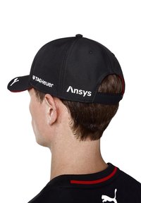Czarna czapka z wygiętym daszkiem, z logo TAG Heuer z przodu i Ansys z boku, oraz czerwonym akcentem na wewnętrznej podszewce.