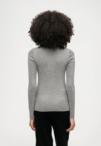 Εφαρμοστό μ�πλουζάκι με μακριά μανίκια σε ανοιχτό γκρι ραβδωτό ύφασμα, με ευθεία τελείωση και λεπτούς καρπούς. Η πίσω όψη εμφανίζει έναν ομαλό, μινιμαλιστικό σχεδιασμό.