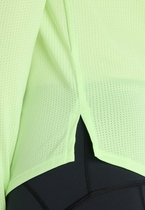 Ljusgrön, perforerad sporttröja med delad fåll, lager-på-lager över svarta kompressionsleggings med kontrasterande sömmar.