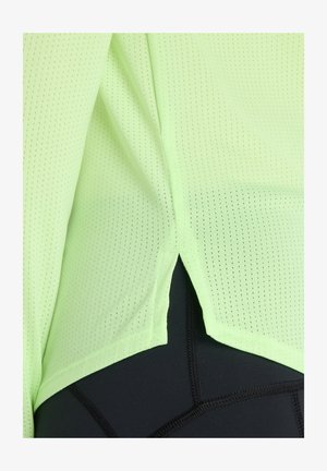 Lichtgroen, geperforeerd sportshirt met een gespleten zoom, gedragen over zwarte compressiebroeken met contrasterende naden.