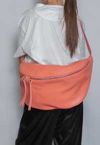 Grande borsa a spalla in pelle corallo con una texture liscia, dotata di una cerniera superiore e due tirazip decorativi. Il design è arrotondato e morbido.