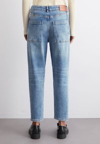 Vaaleansiniset farkut suoralla istuvuudella, joissa on kaksi takataskua ja nahkainen merkki vyötäröllä. Kankaan pintakuviointi ja haalistuneet yksityiskohdat.