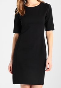 Musta polvipituinen mekko lyhyillä hihoilla, vartalonmyötäinen malli, pyöreä pääntiellä ja sileä pinta, sopii erilaisiin tilaisuuksiin.