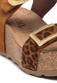 Sandale à plateforme en suède marron avec une sangle imprimée léopard et un accent en boucle dorée. Semelle en liège avec une finition texturée pour une meilleure adhérence et un soutien optimal.