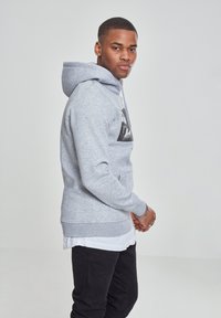 Gray hooded sweatshirt featuring a front kangaroo pocket and a large graphic print on the chest. Worn with black pants and a white shirt underneath.