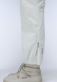 Lightweight, white waterproof pants with elastic cuffs and side zippers. Paired with beige waterproof boots featuring laces and branding.