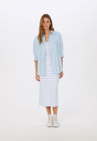 Himmelblaues Hemd über einem maxi Kleid mit weißen und hellblauen Streifen. Kombiniert mit weißen Turnschuhen. Glatter Stoff und lässiges Design.