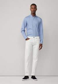 Lichtblauwe overhemdd met een zak, witte jeans en zwarte sneakers. Het shirt heeft lange mouwen en een klassieke kraag.
