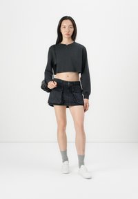 Svart cropped sweatshirt med lange ermer, kombinert med et svart denimskjørt med lommeapplikasjoner. Hvite sneakers og grå sokker fullfører antrekket.
