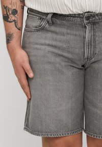 Shorts griși din denim pentru bărbați, cu croială dreaptă, dotate cu buzunare frontale, închidere cu fermoar și margine curată. Material texturat cu un finisaj decolorat.