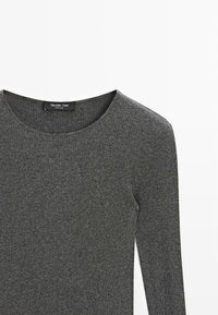 Maglietta grigia a maniche lunghe con scollatura rotonda. Realizzata in un materiale testurizzato, presenta sottili linee orizzontali. Etichetta del marchio visibile.