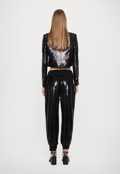 Zwarte pailletten cropped jas en bijpassende broek met elastische tailleband. De jas heeft knoopaccenten; de broek heeft elastische boorden bij de enkels.