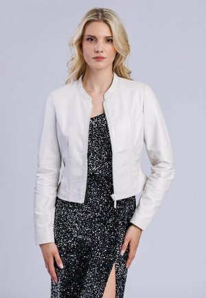 Veste courte en cuir blanc avec un col rond, fermeture éclair et finition texturée, portée sur une robe noire à sequins avec une fente sur la cuisse.