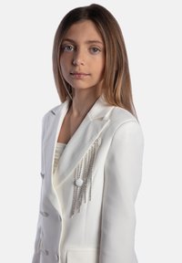 Blazer bianco su misura con un design doppiopetto, caratterizzato da un'ornamentazione testurizzata di catene e perline sulla spalla sinistra.
