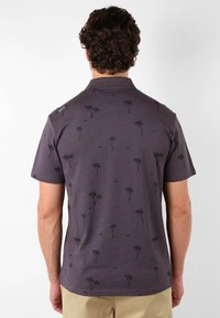 Chemise à manches courtes en tissu gris foncé, présentant un motif de palmier et une texture subtile. Design avec col et détails de couture sur les épaules.