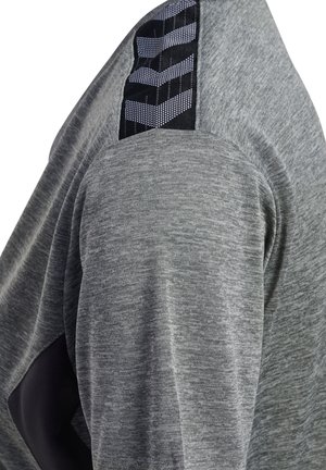 Grå langærmet skjorte med tekstureret stof, med sort accentpanel på skulderen og mønsterdetaljer på skulderpartiet.