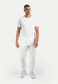 Camiseta blanca de manga corta con cuello redondo y un logo en el pecho, combinada con pantalones jogger blancos a juego y zapatillas blancas.