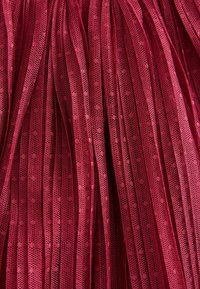 Tissu plissé rouge avec une texture fine en maille, présentant des motifs de tissage ouvert et des lignes verticales, créant de la profondeur et un intérêt visuel.