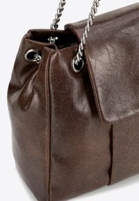 Bruine nep leren tas met een geplooid ontwerp, zilveren kettinghengsel en oogjes. Beschikt over een zachte, gestructureerde oppervlakte.