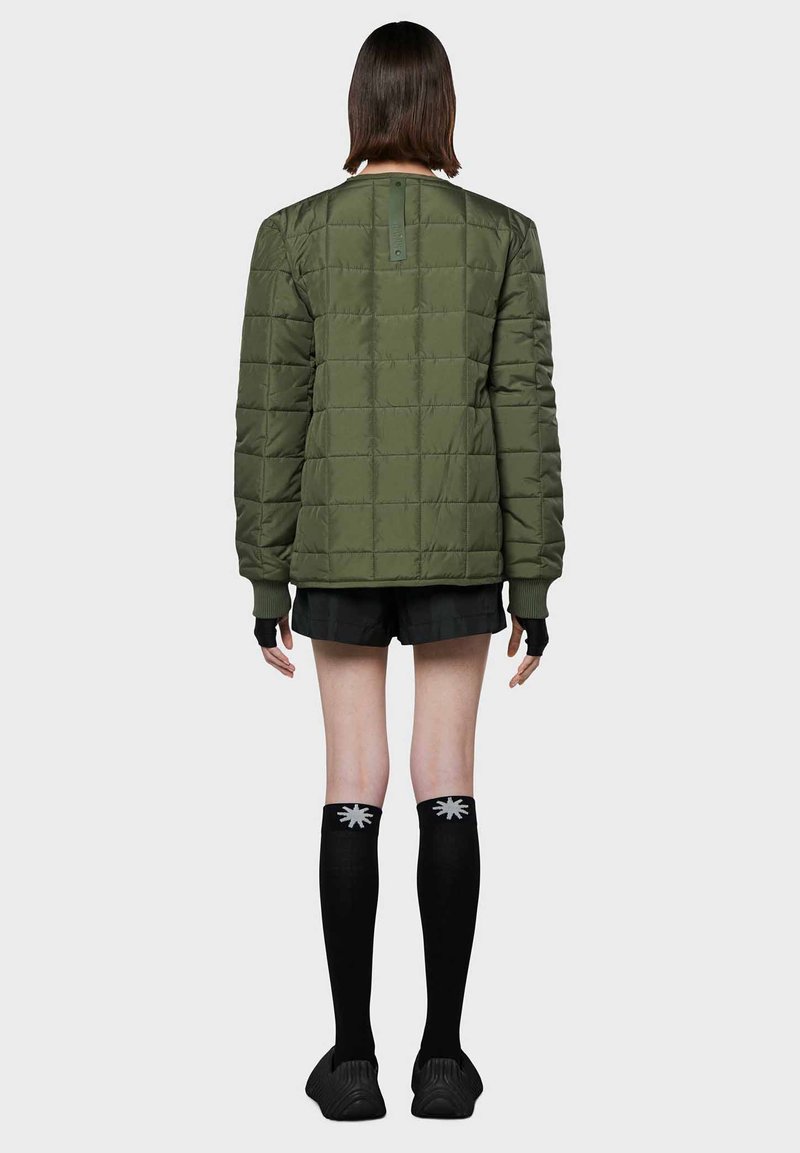 Giacca a vento imbottita verde, con collo rotondo, maniche lunghe e polsini a coste. Abbinata a pantaloni corti neri e calze al ginocchio.