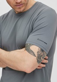Šedé sportovní tričko s krátkým rukávem a texturovaným vzorem. Na levém rukávu je decentní logo "NORTH BEND".