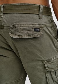 Olivengrønne cargo shorts med en struktureret talje, store sidelommer og et lille mærke syet på baglommen.