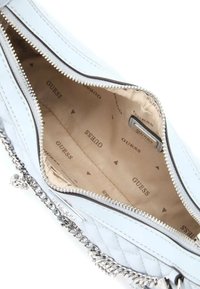 Lichtblauwe quitled handtas met zilveren kettingriem, ritsluiting en een beige interieur met herhaaldelijk "GUESS" logo-patroon.
