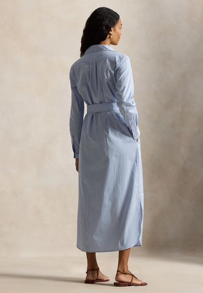 Μακρύ μπλε και λευκό ριγέ πουκάμισο-φόρεμα με ζώνη στη μέση, μακριά μανίκια και κούμπωμα με κουμπιά στο πίσω μέρος, συνδυασμένο με καφέ σανδάλια.