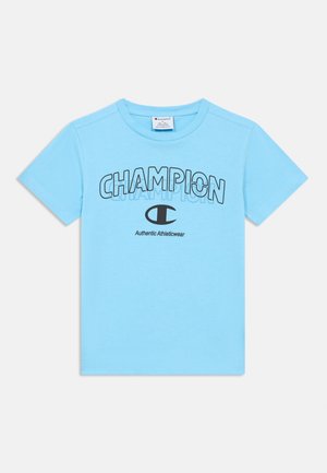 Camiseta de algodón azul claro con mangas cortas, con el texto destacado "CHAMPION" y un pequeño emblema, cuello redondo y textura suave.