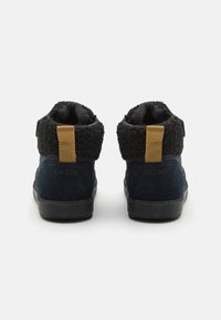 Tmavě modré vysoké tenisky s černým fleecovým límcem, s béžovým poutkem a texturovanou gumovou podrážkou. Jednoduchý, moderní design.