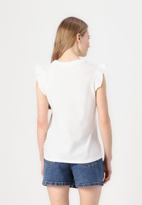 Tricou alb cu mâneci volan, guler rotund și o textură moale, asortat cu pantaloni scurți din denim albastru cu margine tăiată și buzunare spate.