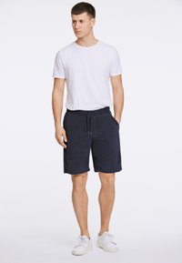 Mörkblå frottéshorts med elastiskt midjeband och sidofickor, ihopparat med en åtsittande vit bomullströja och vita sneakers.