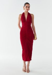 Raudona halter tipo suknelė su raukšlėta tekstūra, vidutinio ilgio, prigludusi siluetas, pagaminta iš minkštos medžiagos. Derinama su auksine rankine ir šlepetėmis.