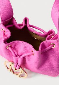 Ροζ δερμάτινη τσάντα με υφή κόκκων, άνοιγμα με κορδόνι και χρυσούς μεταλλικούς τόνους, με εμφανές λογότυπο στο μπροστινό μέρος.