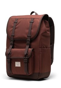 Brown fabric backpack with two front straps, a top flap, front pocket, and mesh back. Features a rectangle logo label on the front.