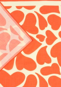 Motif de cœurs orange sur un tissu blanc avec un coin replié, révélant une version rose plus claire du même motif de cœurs en dessous.