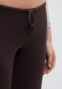 Tumepruunid retuusid pehmest kangast, millel on nööriga vöökoht. Disainil on sile tekstuur ja keha järgnev vorm.