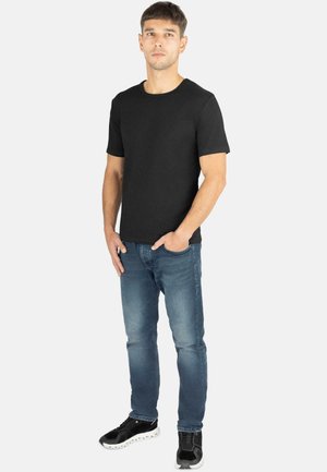 Schwarzes Baumwoll-T-Shirt mit Rundhalsausschnitt, kurzen Ärmeln und einem dezenten Logo, kombiniert mit blauen Jeans und schwarzem Schuhwerk.