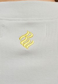 Grå ribbet stoff har en gul brodert logo på baksiden. Teksturen er glatt med tydelige horisontale linjer.