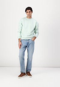 Mintgrøn sweatshirt, lyseblå jeans, brune sneakers. Sweatshirten har rund hals og ribbede manchetter. Enkel, afslappet pasform.