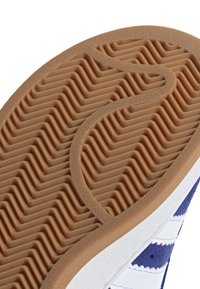 Skoesåle med et teksturert, ribbet design i lysbrunt gummi. Siden har hvite og blå paneler med hvite striper.