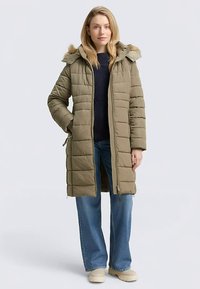 Olijfgroene gewatteerde jas met een afneembare capuchon met bontafwerking. Voorzien van een ritssluiting aan de voorkant, grote zijzakken en een knielang ontwerp.