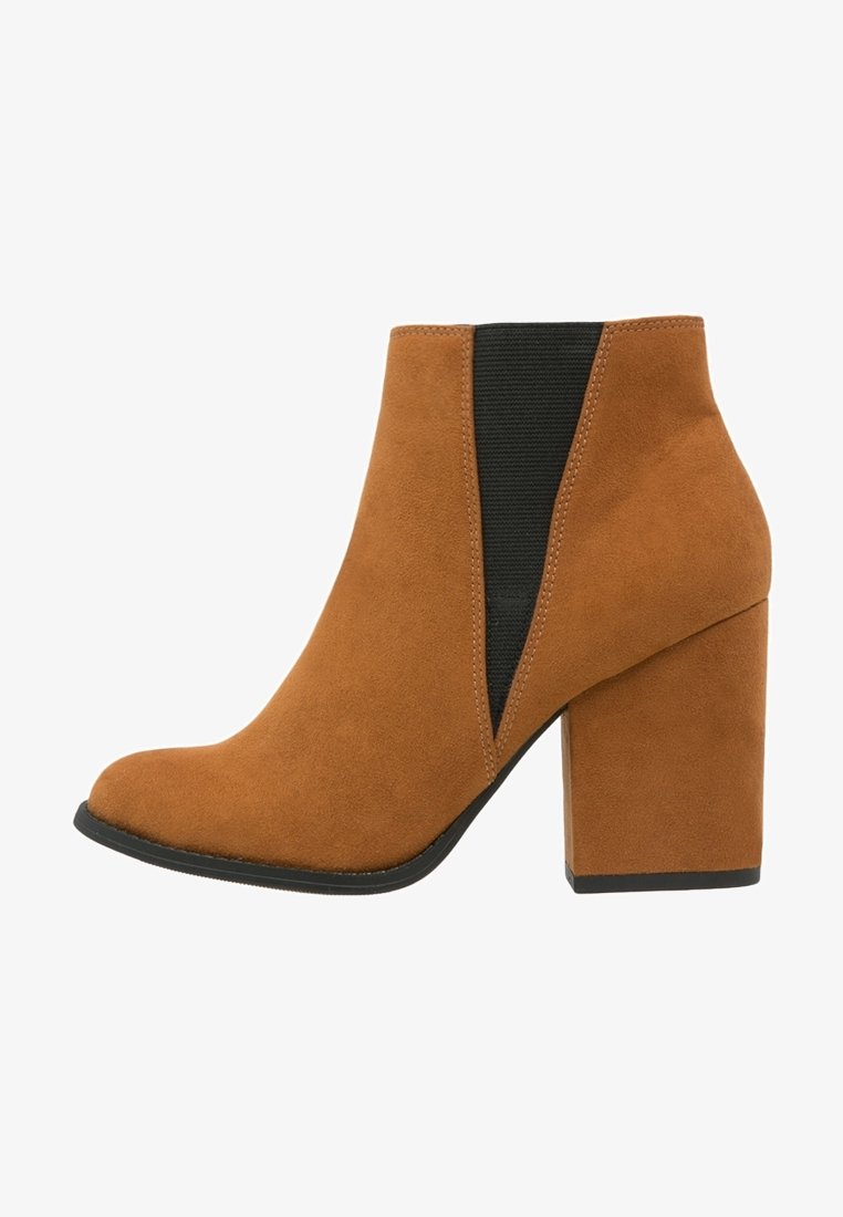 Bottine en daim beige pour femme avec talon block, panneau latéral élastique noir, bout angulé et semelle noire.
