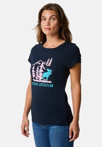 Laivansinisestä puuvillapaidasta, jossa on graafinen printti vuorista ja hirvestä vaaleanpunaisena ja turkoosina. Lyhyet hihat, pyöreä kaula-aukko.